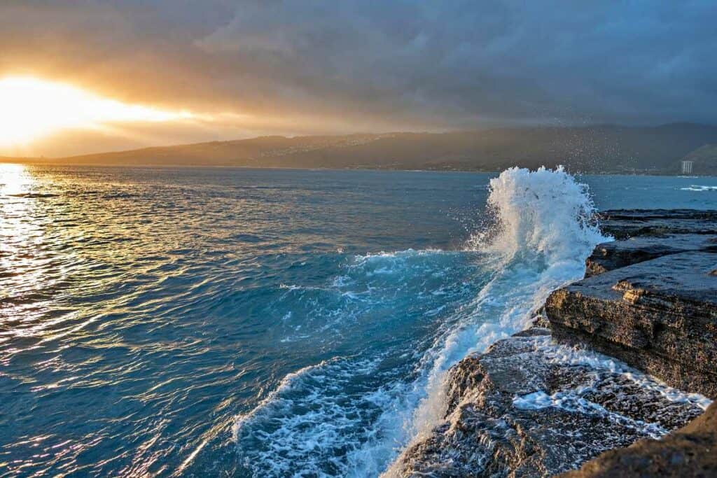 Sunset from China Walls, Oahu, with waves crashing into the cliffs