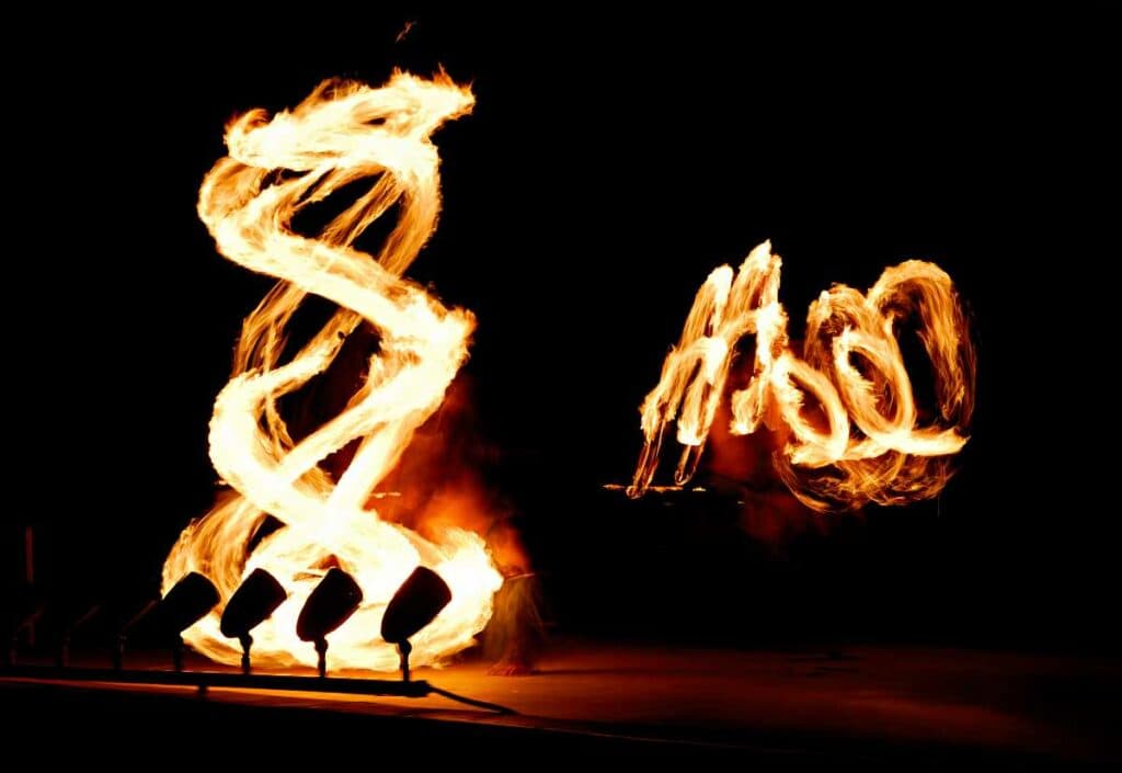 Pair of fire dancers spinning lit batons at night after a luau
