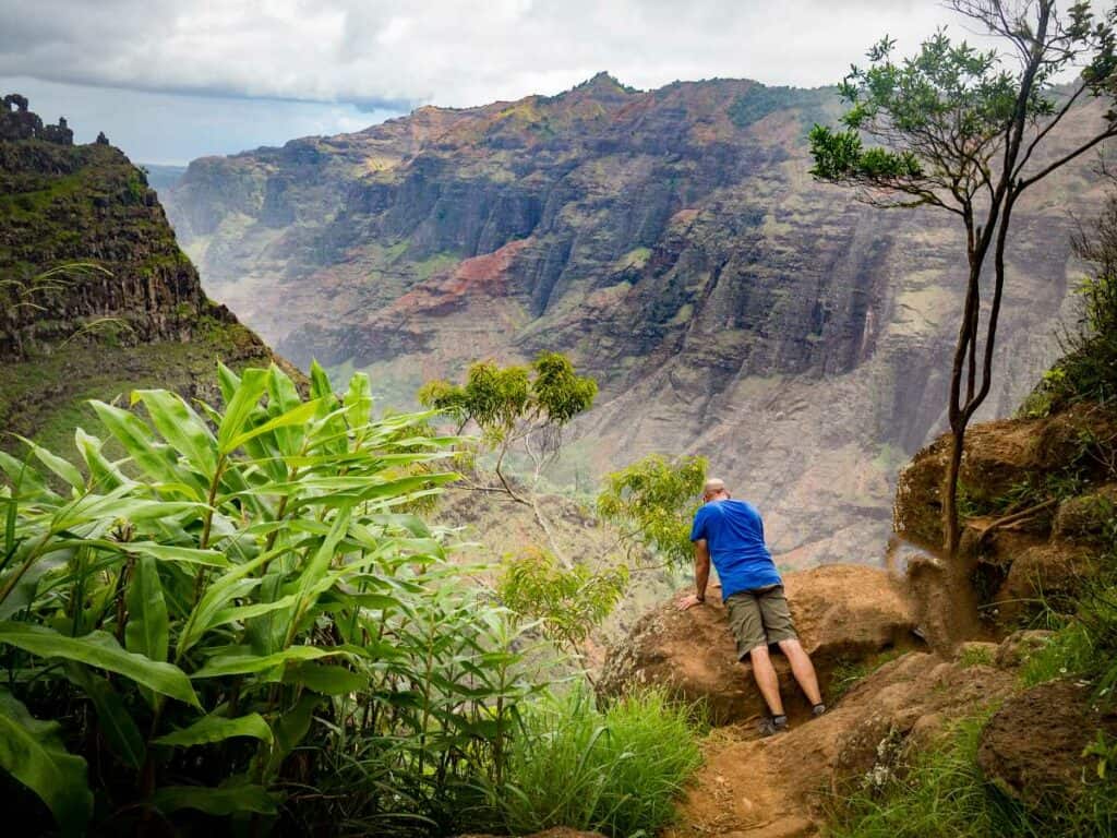 Peering over the cliff to see the 800-foot waterfall from the Canyon Trail to Waipo'o Falls, Kauai, HI