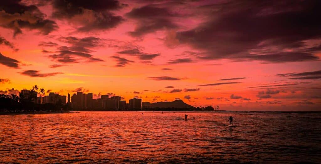 Ala Moana Beach paddle boarders and surfers returning at sunset, with the Honolulu skyline and Diamond Head crater framed in the background