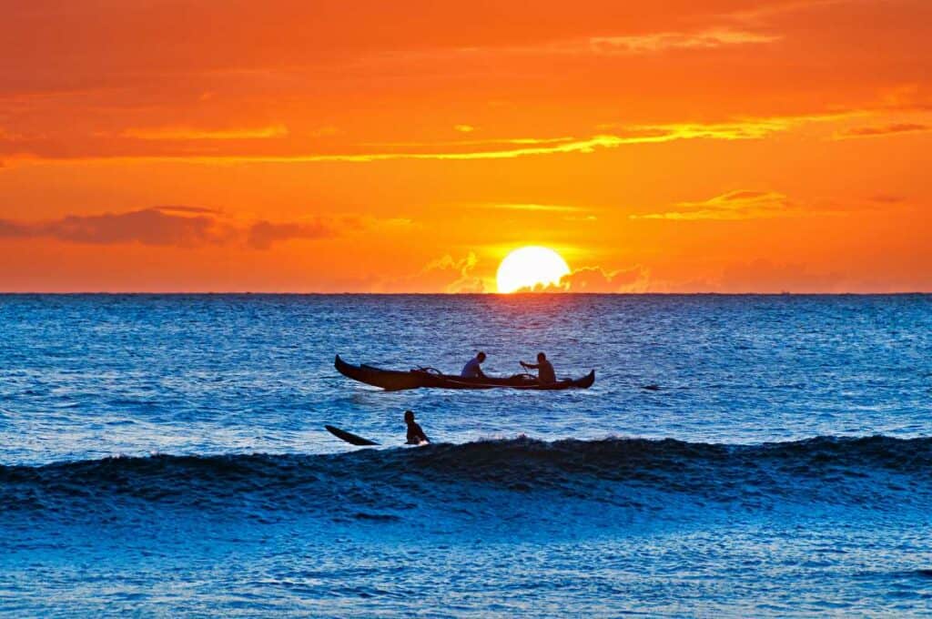 Surfer waiting for wave at sunset, with outrigger canoe in the background at Ka'anapali Beach, Maui, HI