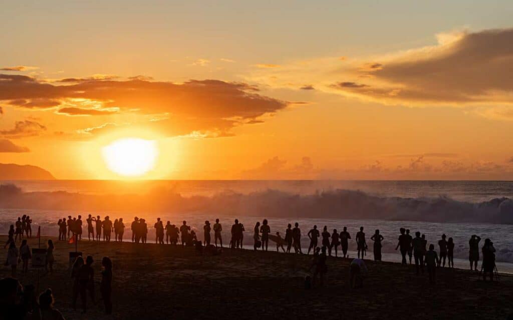 Crowd of surfing spectators treated to a stunning sunset over the Banzai Pipeline at Ehukai Beach Park, Hawaii